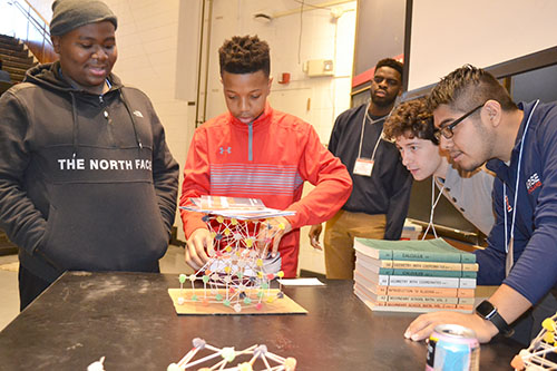 llinois engineering students (right) watch as two Chicago seventh graders test their structure by piling books on it.