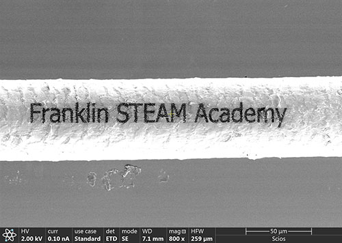 A piece of hair etched with the Franklin logo using a focused ion beam. Dr. Honghui Zhou, an MRL staff scientist who runs this instrument, helped the middle school students etch this and then image it.