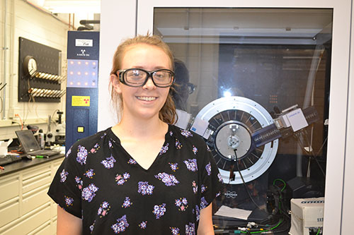 I-MRSEC undergrad Carmen Paquette by one of the instruments she used during her research  in the synthesis of antiferromagnetic material this past summer in Professor Daniel Shoemaker's lab.