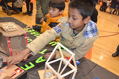 A STEAM night visitor ratchets up the shaking while testing the earthquade structure he built.