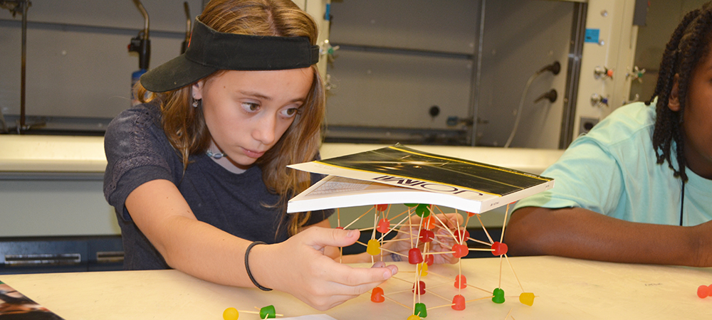 A Mid-GLAM camper tests her team's toothpick/gumdrop structure. Mid-GLAM is one of the many camps available at Illinois during the summer