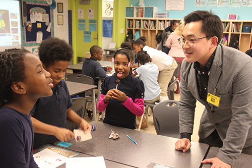 Jiho Kim interacts with BTW fourth graders as the students either rub their suckers on sandpaper and/or lick them as part of his corrosive wear activity. (Photo courtesy of Joe Muskin.)