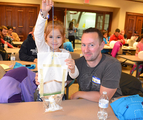 A young visitor shows off the egg-drop contrivance she and her dad designed. Her egg was one of the few that made it through the test without a crack.