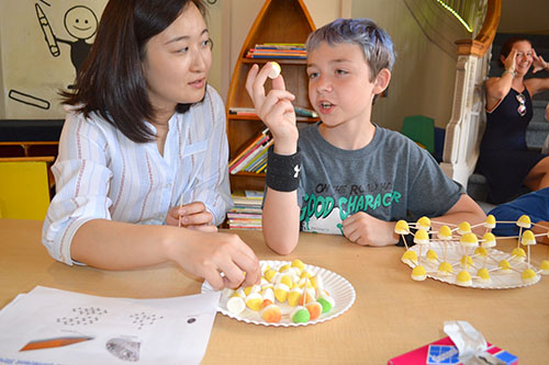 Lili Cai discusses with a child how to arrange the gum drops to form the shape of a molecule.