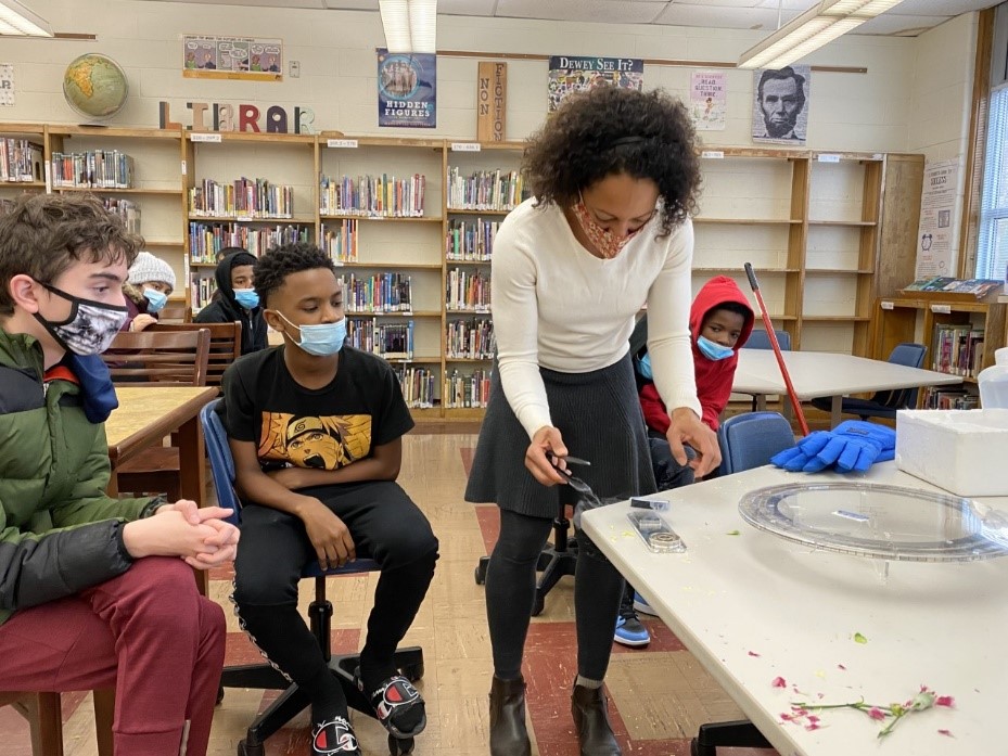 Mason holds up two beakers of water, demonstrating to students what happens when dye is dropped into steaming hot water and a frigid cold water.