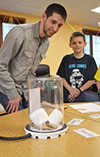 Tyler Haddock (left) and a STEAM Studio student watch as two marshmallows expand as a vacuum is created in the bell jar.