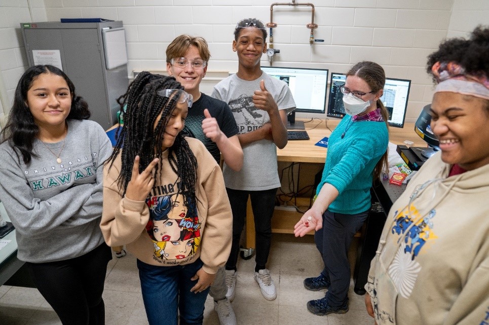 Dr. Kathy Walsh, third from right, and a group of middle schoolers at the 3D Optical Profilometer, show off the candy samples they studied. (Photo by Heather Coit).