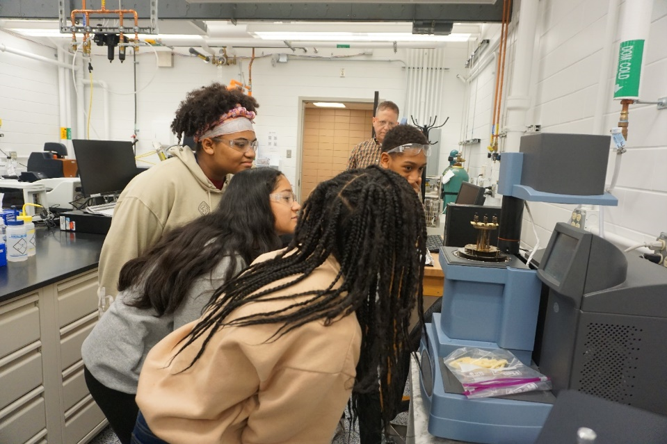Top photo: A group of middle schoolers eagerly watch for the snack food to snap, during an activity led by Dr. Roddel Remy, at back right. (Photo by Pamela Pena Martin.)