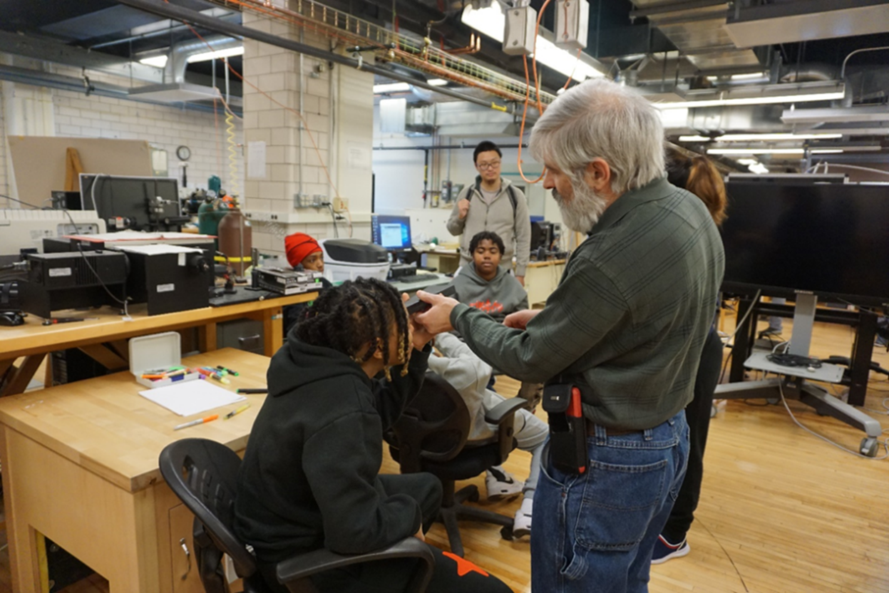 At right, Dr. Julio Soares helps a middle schooler view light through a spectrometer that separates light into its components. (Photo by Pamela Pena Martin).