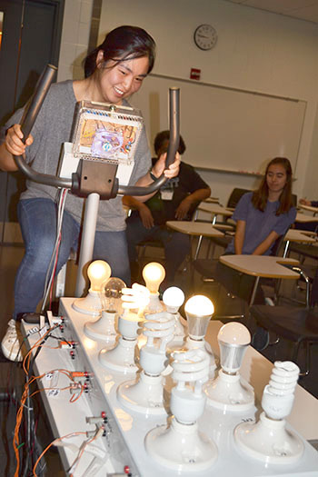 Elizabeth Ohr, Urbana High School Science teacher, helps out with a demonstration by pedaling a stationary bike in order to make the light bulbs glow.