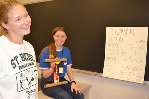 Students in the Cardboard Group present their poster, Digiorno Vs. Disposal, and the prototype hanger they designed which repurposes cardboard.