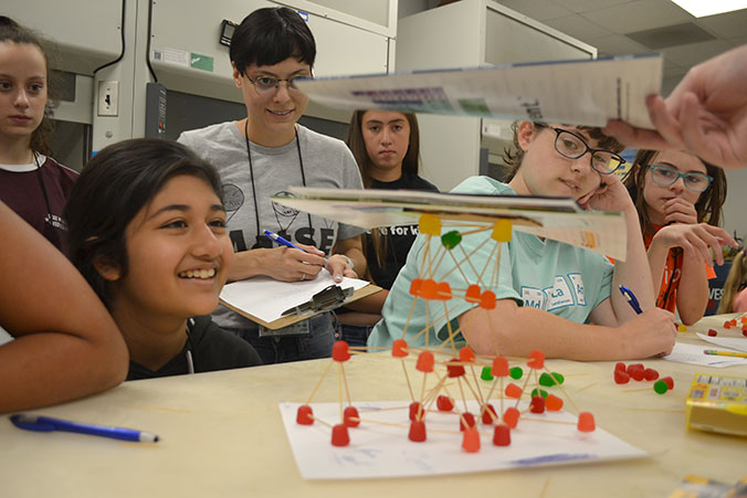 Mid-GLAM campers and lab assistants watch as journals are piled on one team's structure during testing.