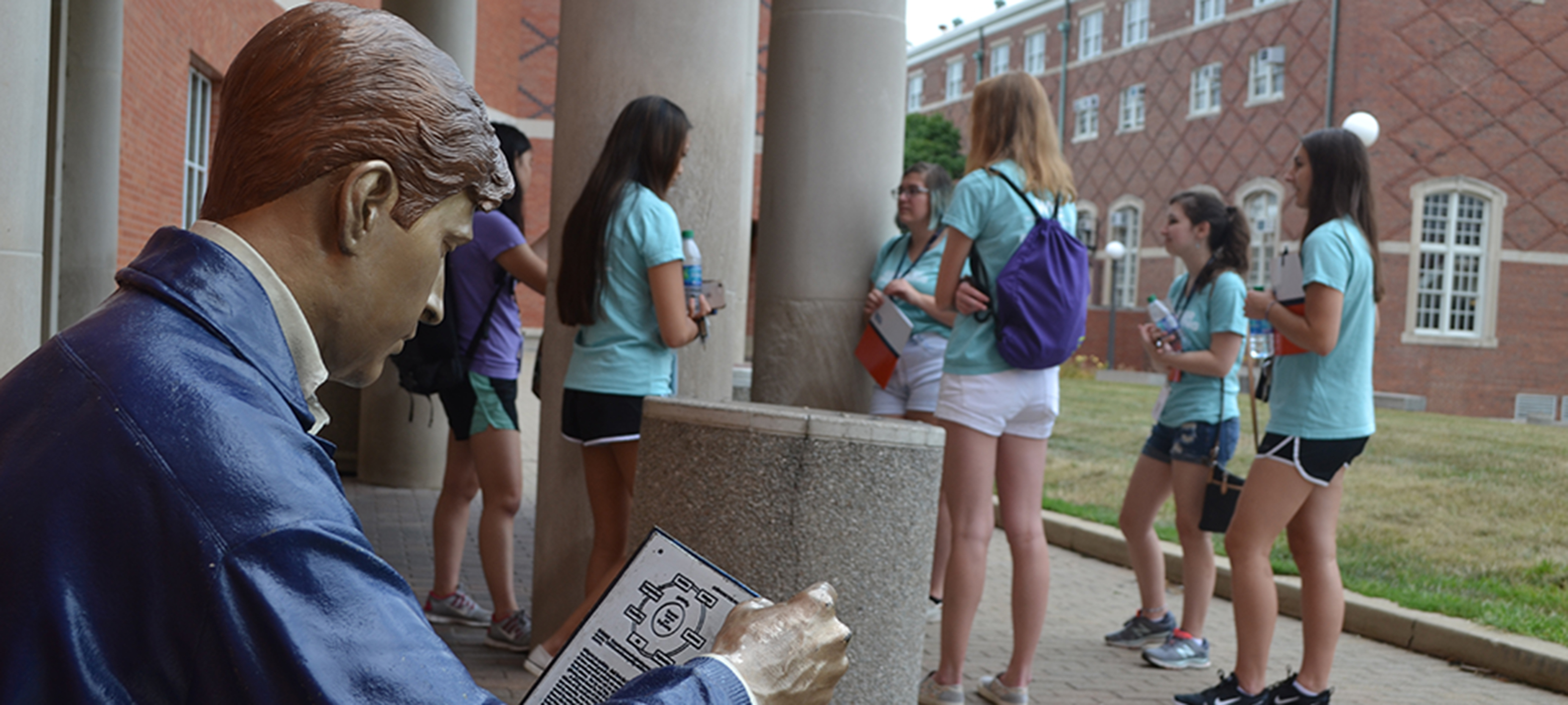 At the fall 2019 WIE Orientation, a group of female engineering freshmen chat on the south portico of Grainger Library as Grainger Bob looks on.