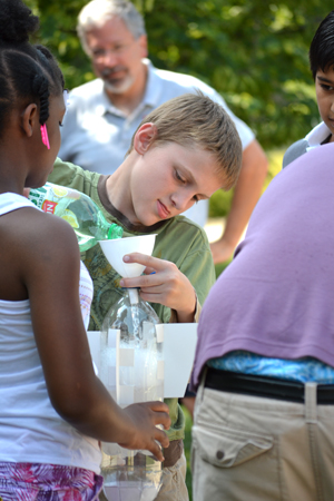 Campers prepare bottle rocket for launch as Bob looks on.