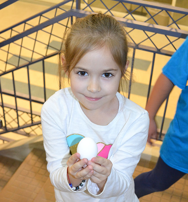 A young girl proudly displays the egg she safely dropped from the second story to the first with nary a crack due to the excellent device she and her father designed