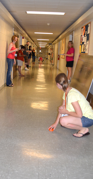 Teachers wait to measure velocity of a puck the teacher in the foreground is going to send skidding down the hall.