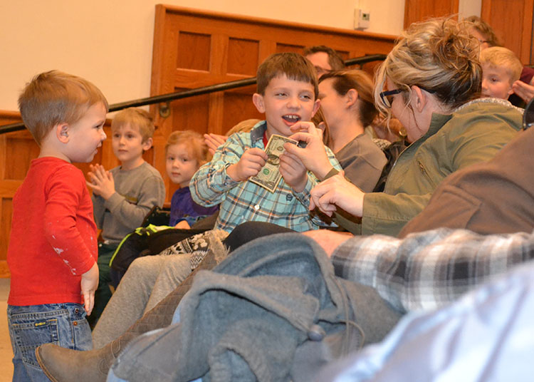 A young boy shows his mom the dollar bill he got which had been "on fire" but hadn't burned up.