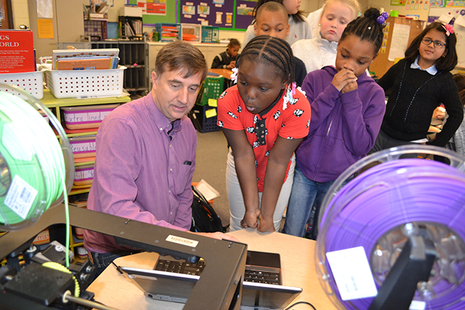 Joe Muskin (left) and several King students watch as a 3D printer cranks out the keychains they designed.