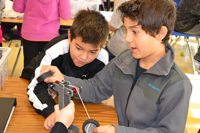 Two fourth graders analyze which works better for lifting the tires: two pulleys or three.