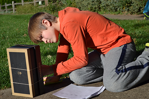 A student takes a reading on one of the thermometers on his  sling psychrometer.