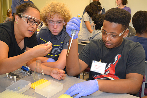 Paola Estrada works with a UHS student using a pipette to get a DNA sample